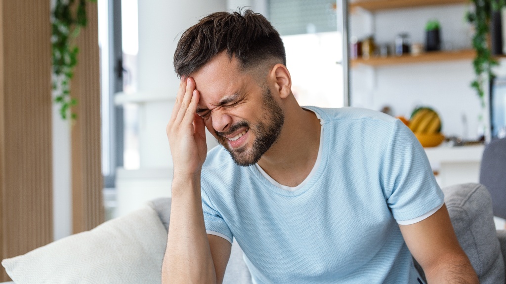 young man suffering from headache at home, touching his temples