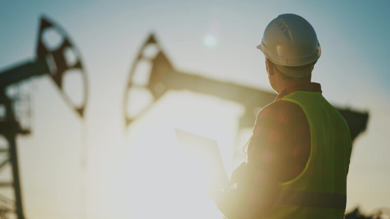 worker works next to an oil pump holding a laptop