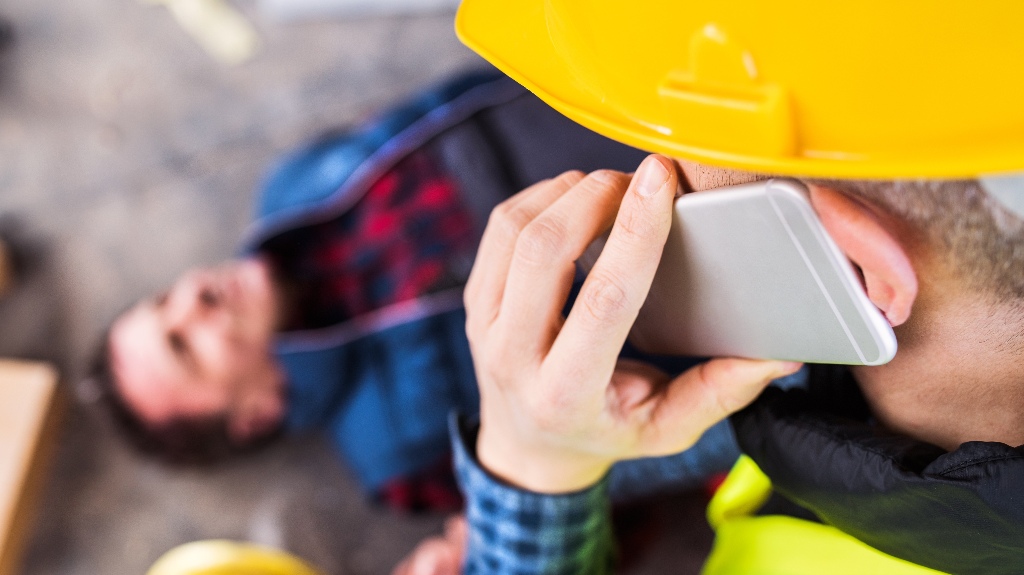 Colleague giving first aid to unconscious worker after accident, calling ambulance